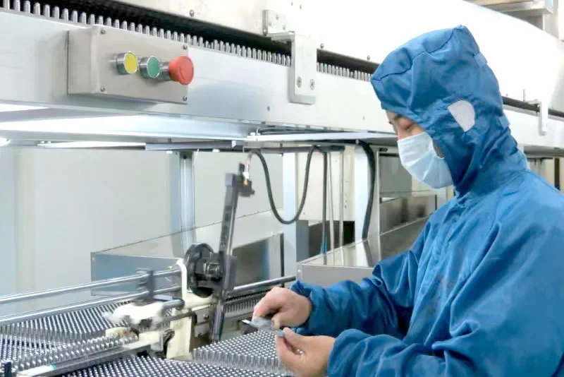 Gowned operator inspecting capsule blister packs at filling line